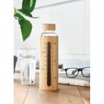 Botella de vidrio con funda y medidor color madera vista bodegón